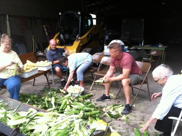 Family sitting in chairs shucking sweet corn 